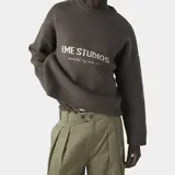 Sweater de punto color marrón oscuro, de manga larga y corte oversize, con cuello redondo y el logotipo de la marca estampado en el pecho en tono claro.