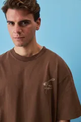 Remera marrón oversize de manga corta, con cuello redondo y pequeño estampado gráfico en el pecho.