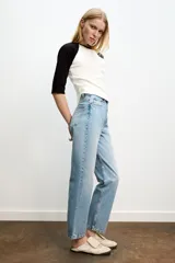Jeans de mujer, tiro alto, color azul medio con efecto desgastado (lavado claro en muslos y oscuro en bordes). Corte recto y ancho (mom fit) con cinco bolsillos y cierre frontal de botón y cremallera.