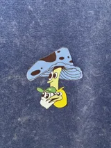 Remera de algodón premium color negro con efecto lavado, de manga corta y corte holgado. Presenta un estampado gráfico en la espalda con el texto 'Good Trips, Good Friends' y una ilustración de personajes apilados.