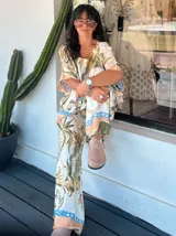 Blusa de satén con estampado de cadenas y hojas en tonos blanco, marrón y negro. Tiene corte amplio, mangas cortas y cuello redondo. Se ajusta a la cintura con un cinturón elástico negro con hebilla dorada.