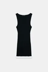Vestido corto de punto canalé negro, con cuello barco, sin mangas y detalle de volados blancos en el borde inferior.