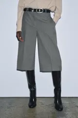 Bermuda larga gris confeccionada en hilatura con viscosa, de tiro medio y cintura con trabillas. Presenta bolsillos laterales ocultos en costura, detalle de raya plancha y cierre frontal con cremallera, botón y ganchos metálicos.