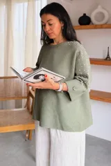 Sweater gris melange con detalles de perlas y strass aplicados en las mangas, de corte holgado y mangas largas.