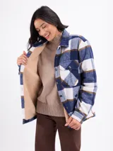 Sobrecamisa de corte holgado con estampado de cuadros en tonos azul, blanco y marrón. Presenta cierre frontal con botones, cuello clásico, bolsillos en el pecho y un interior forrado en sherpa color beige.