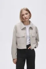 Chaqueta de eco-cuero en color beige, con diseño holgado, cuello tipo camisa y cierre frontal metálico. Presenta dos bolsillos frontales con solapa y mangas largas con puños rectos.