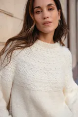 Buzo tejido de punto con cuello redondo, manga larga y diseño holgado. Presenta tajos laterales y un corte asimétrico, siendo ligeramente más largo en la parte posterior.