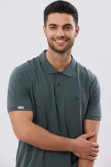 Remera polo de manga corta, color verde oscuro, confeccionada en tejido de jersey. Presenta cuello camisero con botones y bordado sutil en el pecho.