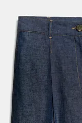 Pantalón ancho de mezclilla azul oscuro, tiro medio, con pinzas delanteras y pespuntes a contraste. Presenta cierre frontal con botón y cremallera.