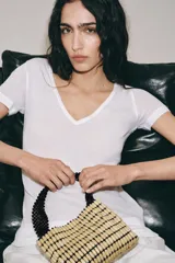 Mini bolso cuadrado confeccionado con cuentas de madera en tonos tostados y asas de mano rígidas con aplicación de abalorios negros a contraste.