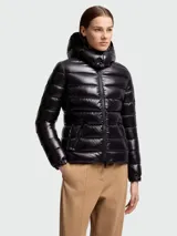 Campera puffer corta de nylon laqué color negro, con relleno de plumas, capucha desmontable, cierre frontal con cremallera y bolsillos laterales con cremallera.