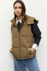 Chaleco puffer acolchado color verde oliva, con cuello alto, capucha desmontable y cierre frontal. Cuenta con bolsillos laterales funcionales.