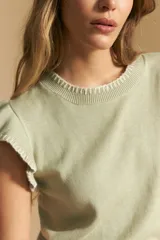 Top tejido sin mangas color negro, con cuello redondo y volados en las sisas con terminación en contraste de punto blanco. Presenta un calce recto y puño inferior acanalado con detalle de punto blanco.