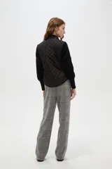 Chaleco negro con diseño capitoneado, cierre frontal con botones a presión y cuello alto.