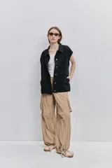 Chaleco de jean negro, de calce relajado con hombros caídos, cuello camisero, cierre frontal con botones y grandes bolsillos aplicados.