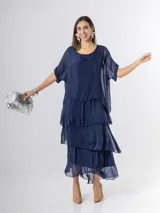 Vestido largo azul marino de seda italiana, con diseño de volados escalonados en la falda y una sobrecapa superior con mangas cortas amplias.