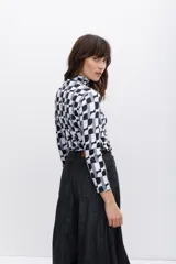 Polera de poliéster color beige con estampado geométrico en negro. Tiene cuello alto y mangas largas.