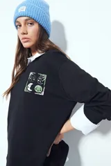 Remera de manga larga negra con cuello redondo y puños blancos visibles, presentando un estampado gráfico con motivos celestiales en el pecho.