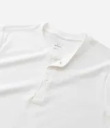 Remera masculina blanca de manga corta, con cuello redondo y abertura frontal con botones. Confeccionada en algodón y poliéster con textura, de corte ajustado.