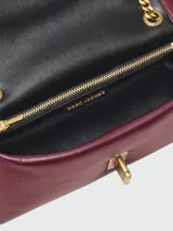 Cartera Marc Jacobs modelo The Puffy Smooth Dual Chain Mini Bag, confeccionada en cuero liso de color bordó, con diseño acolchado y solapa frontal. Cuenta con cierre de broche metálico dorado y correa de cadena metálica doble.
