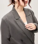 Blazer sastrero oversize color gris, de doble botonadura cruzada, solapas anchas, bolsillos delanteros embutidos y mangas largas.