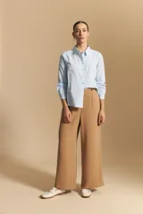 Camisa de corte clásico y holgado, confeccionada en tela blanca, con cuello camisero, cierre frontal de botones de nácar y mangas largas con puños abotonados.