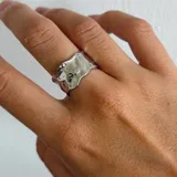 Anillo plateado con diseño irregular y superficie texturizada.
