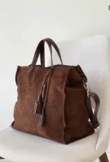 Bolso marrón de gamuza con textura efecto cocodrilo, doble asa de mano y correa ajustable extraíble de cuero. Cuenta con detalle de borlas colgantes en el frente.