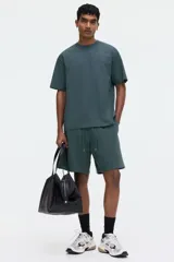 Remera verde oscuro de corte relajado, confeccionada en punto de algodón de peso medio, con cuello redondo ribeteado y hombros caídos.