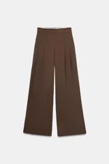 Pantalón de tiro medio color marrón, con pinzas en el delantero, perneras anchas de corte recto y trabillas para cinturón. Cuenta con bolsillos laterales y traseros, y cierre frontal con cremallera y botón.