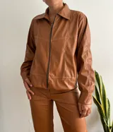 Campera marrón de cuero sintético con cierre frontal, cuello camisero y costuras decorativas en hilo blanco.