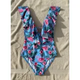 Malla enteriza color celeste con estampado de flamencos y flores tropicales. Presenta escote en V profundo con volados decorativos en los hombros y el frente, y diseño de espalda abierta.
