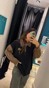 Sweater de punto negro con cuello polo y cierre parcial. Las mangas son de tejido trenzado color marrón, al igual que el cuello. Presenta un aplique bordado en el pecho con forma de hongo.