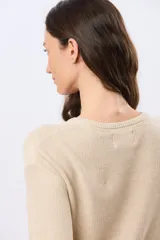 Buzo tejido liso de manga larga con cuello redondo, confeccionado en algodón de tejido grueso. Presenta bordes acanalados en el cuello, los puños y la cintura, con un pequeño detalle de placa metálica en el lateral inferior.