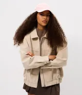 Campera bomber oversized de poliuretano con acabado efecto gamuza en color beige. Presenta cuello camisero, cierre frontal, mangas largas con puños abotonados y ruedo elástico.