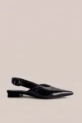 Zapato tipo flat destalonado de color negro con acabado brillante, punta fina y cierre con hebilla lateral.