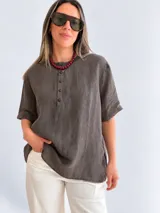 Blusa de lino color beige con cuello redondo, mangas cortas y cierre frontal parcial con botones oscuros.