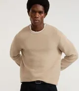 Suéter de punto color beige, con cuello redondo, manga larga y textura maquinetada.