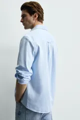 Camisa de corte regular fit confeccionada en tejido de algodón con textura twill. Presenta cuello italiano, manga larga con puños abotonados y cierre frontal de botones.