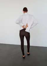 Pantalón slim fit de color marrón oscuro, con diseño largo, cintura elástica y detalle de costuras. Presenta una abertura en el bajo con cierre de cremallera.