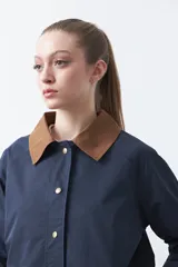 Trench tipo barn jacket color marrón, con cuello camisero en contraste azul marino, cierre frontal con broches y bolsillos amplios. De silueta recta y calce cómodo.