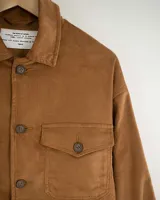 Camisa de pana color beige, de manga larga, con cuello camisero, cierre frontal de botones y dos bolsillos de parche con solapa en el pecho. Presenta un corte recto y holgado.