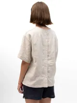 Remera de lino con corte holgado, cuello redondo y mangas cortas. Presenta un diseño minimalista con detalle de botones en la espalda.