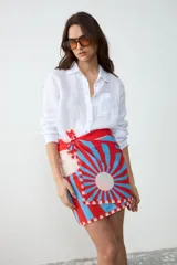 Pareo rectangular estampado con diseño geométrico radial en tonos rojo, celeste y blanco, inspirado en la arquitectura Art Decó. Confeccionado en Uruguay, ideal para usar como falda cruzada, accesorio de playa o chal.