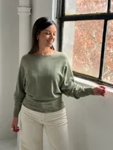 Sweater de punto color verde oliva, con cuello bote y mangas murciélago. Presenta un diseño de textura acanalada vertical en el frente y puños ajustados.