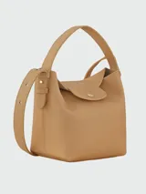 Cartera bucket S Longchamp modelo Le Cadence, confeccionada en cuero granulado color bordó. Presenta solapa frontal con botón a presión metálico dorado y grabado de la marca, asa superior de mano y correa de hombro ajustable y desmontable.