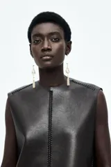 Vestido corto sin mangas en tejido revestido color negro con pespuntes trenzados, escote redondo y cierre oculto en la espalda.