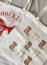 Tote bag de tela tipo lienzo color crudo con estampado de botas texanas y lazos.