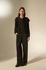 Camisa negra de viscosa con textura arrugada, cuello a la base y cierre frontal con botones. Presenta volados en los hombros y mangas largas.
