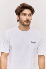 Remera blanca de algodón, de corte holgado y mangas cortas, con pequeño estampado azul en el pecho.